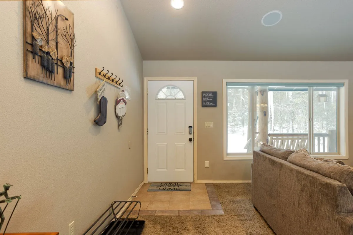 A welcoming foyer with an entrance door, window with a view, cozy sofa, and wall art. The space is bright and inviting, suggesting a warm greeting for every guest—human or canine.