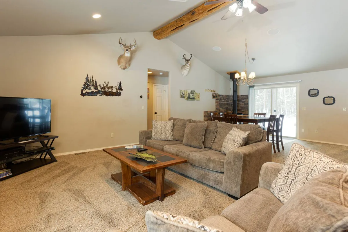 This image showcases a spacious living room with a comfortable sofa, coffee table, flat-screen TV, and a dining table in the background. Decorative deer heads add a warm, rustic touch, and the space feels welcoming and ideal for family gatherings or relaxing evenings.