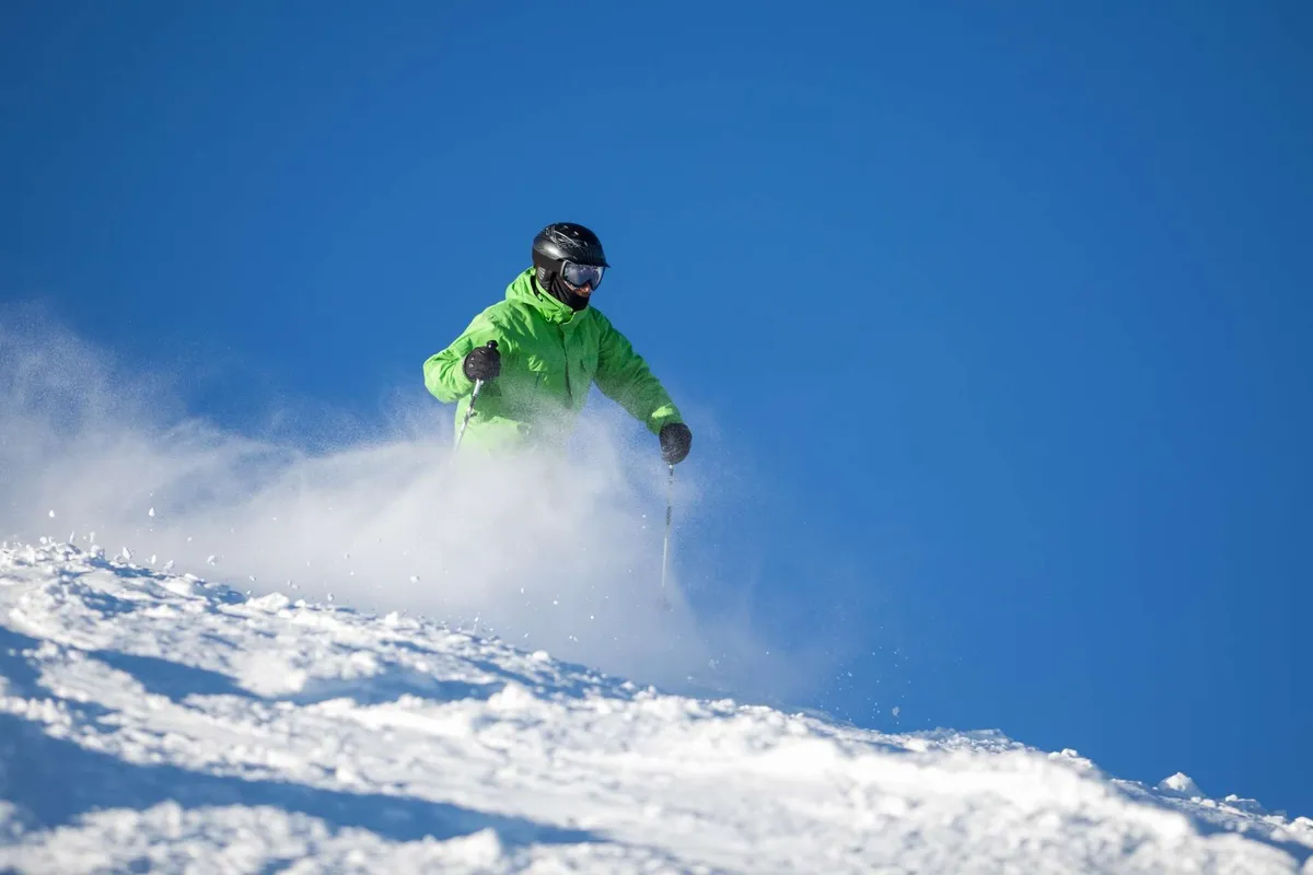 An exterior scene featuring a skier on a snow-covered slope beneath a clear blue sky. The wide open landscape conveys the expanse and beauty of Sunriver's outdoors, inviting active exploration and adventure for guests and their companions.