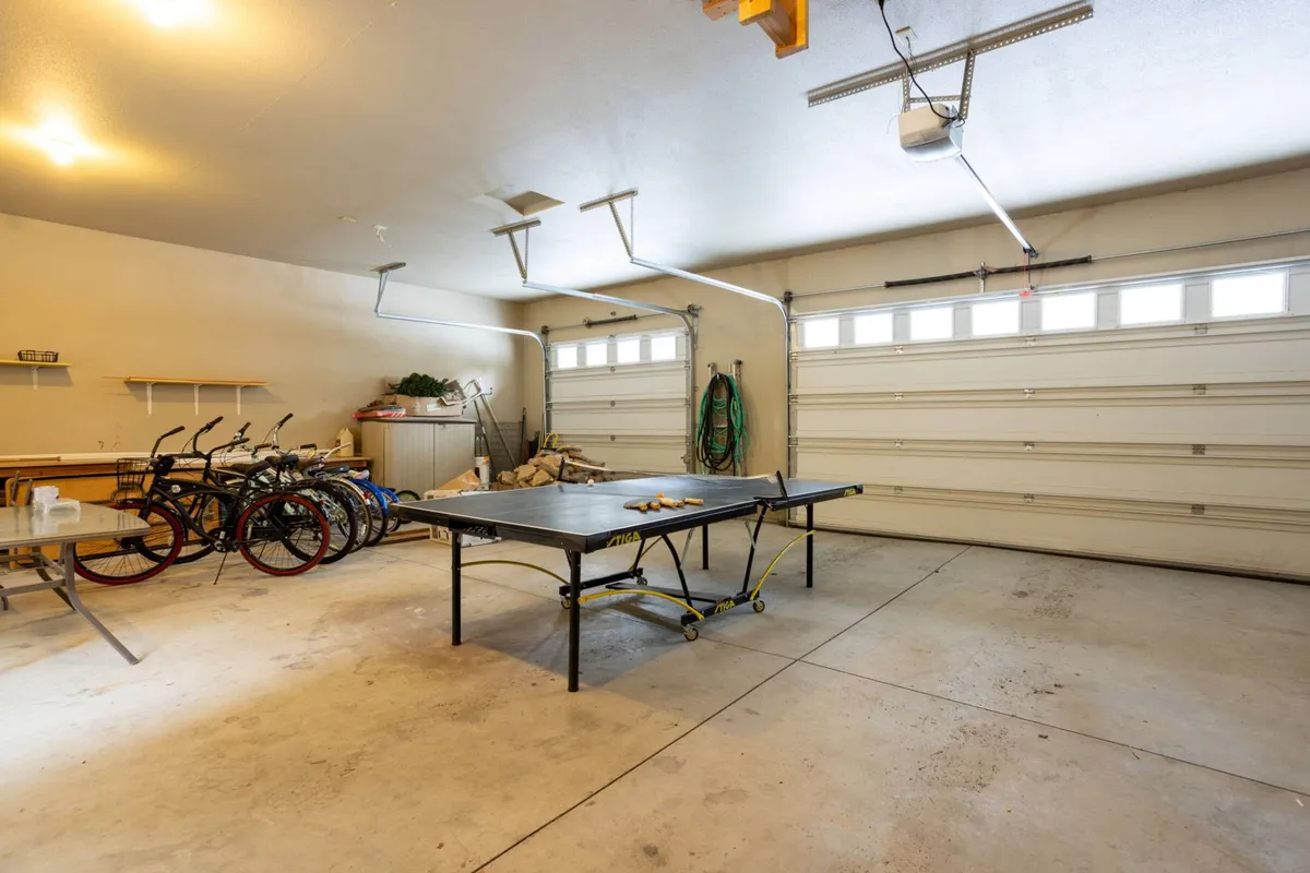 Inside the garage, a ping pong table takes center stage, surrounded by bicycles and organized storage, suggesting a versatile space for friendly matches and shared activities. The space is casual, functional, and ready for both play and preparation for outdoor adventures.