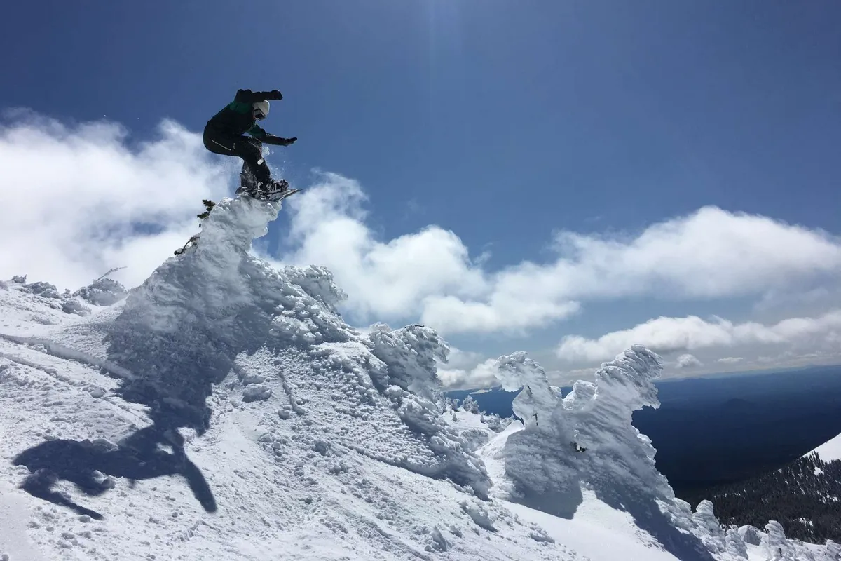 This action shot shows a snowboarder mid-air against a backdrop of a snow-covered mountain peak and dramatic clouds. The image evokes excitement, adventure, and the thrill of winter sports in a beautiful alpine landscape.