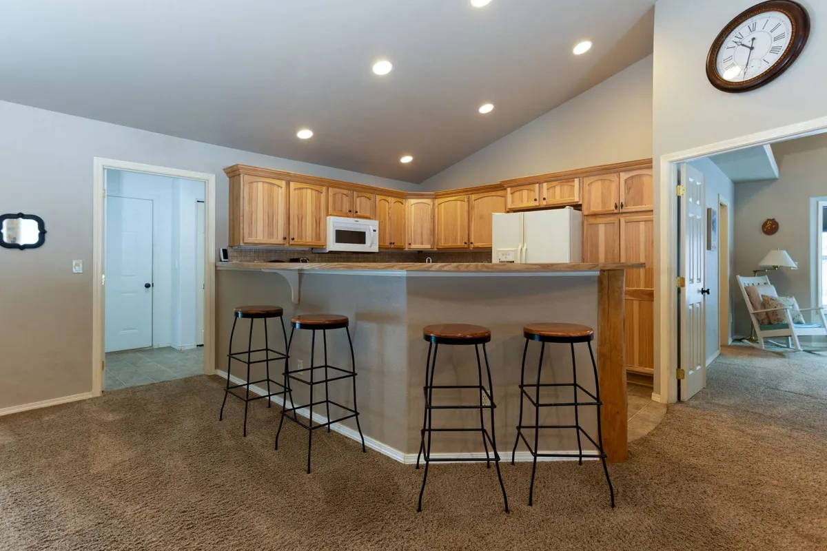 A view of the kitchen featuring a central island with bar stools, wood cabinetry, and stainless steel appliances. The layout is open and inviting, making it easy for people to mingle, prep snacks, or enjoy a casual meal together.