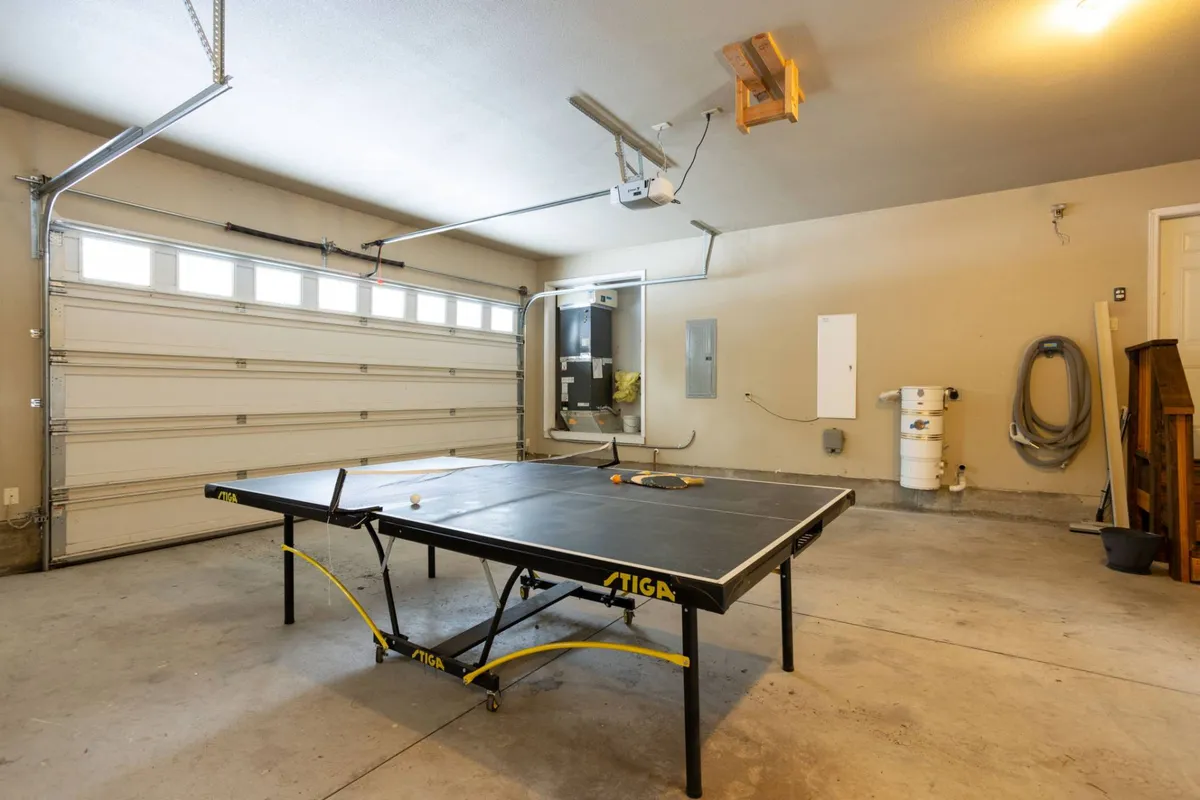 A bright interior view of the garage highlights a ping pong table, open garage door, and ample storage. The playful mood invites friendly competition and illustrates another angle of the game and gathering space.