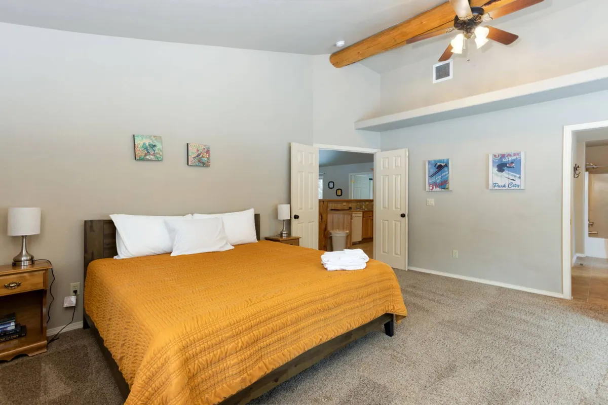 This interior shot showcases a serene bedroom with a bed covered in a bright yellow quilt, rich wooden ceiling beams, and tasteful wall art. The space appears cozy, well-lit, and perfect for winding down after a day of adventure.