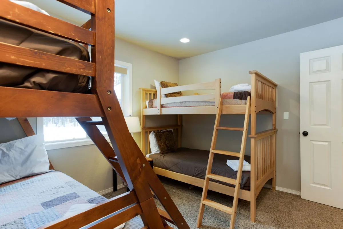 A playful and inviting bedroom with twin-over-full bunk beds, a window that lets in ample daylight, and a lamp for nighttime reading or games. The room feels cheerful and adaptable, perfectly suited to children or groups.