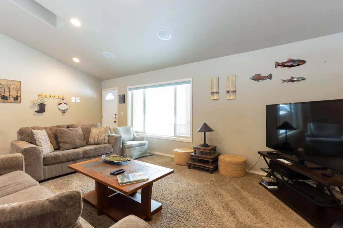 The image showcases a bright, inviting living room with a comfy sofa set arranged around a modern coffee table and a large television. Natural light streams in through a generous window, illuminating playful decorative fish art on the wall. The setting feels perfect for relaxing with loved ones, enjoying a family movie night, or gathering for games in a homey, welcoming atmosphere.