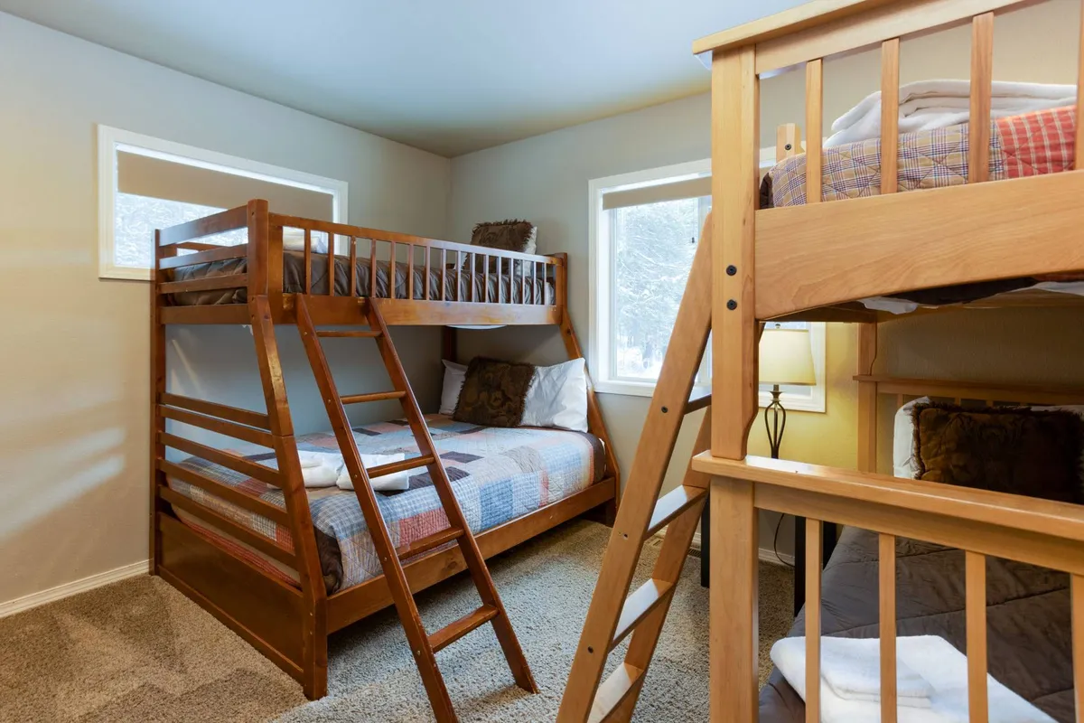 A bunk room with inviting beds, windows that let in natural light, decorative pillows, and a lamp, creating a space ideal for families or groups to unwind and bond after a day outdoors.